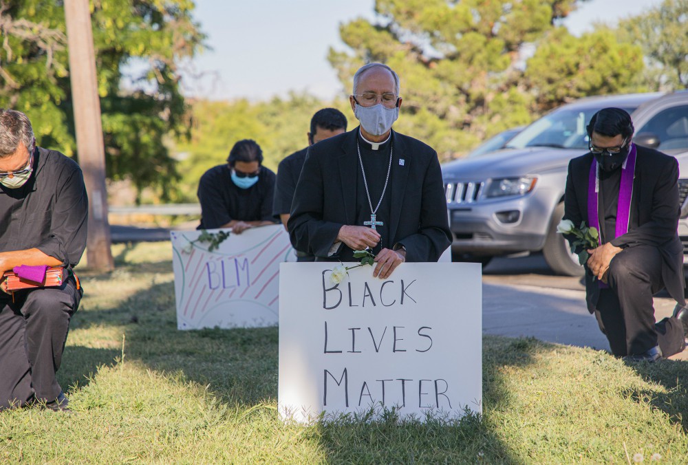 Bishop Mark Seitz of El Paso, Texas, kneels at El Paso's Memorial Park holding a Black Lives Matter sign June 1. (CNS/Courtesy of El Paso Diocese/Fernie Ceniceros)