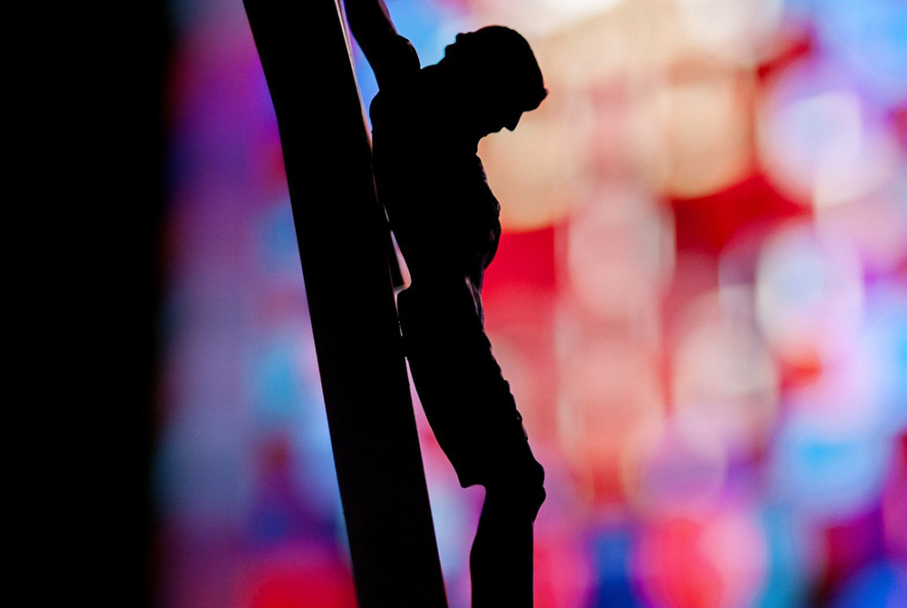 A crucifix is silhouetted against a stained-glass window in this illustration photo. (CNS/Mike Crupi, Catholic Courier)