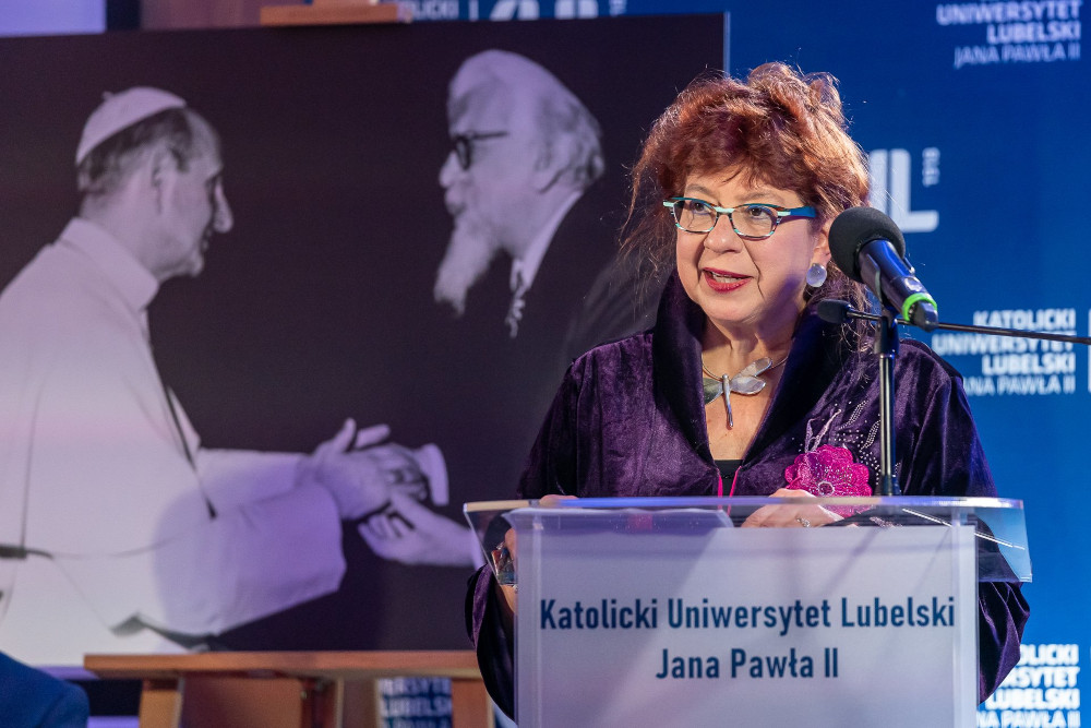 An older white, red-haired woman stands at a podium with the words Katolicki Uniwersytet Lubelski Jana Pawla II