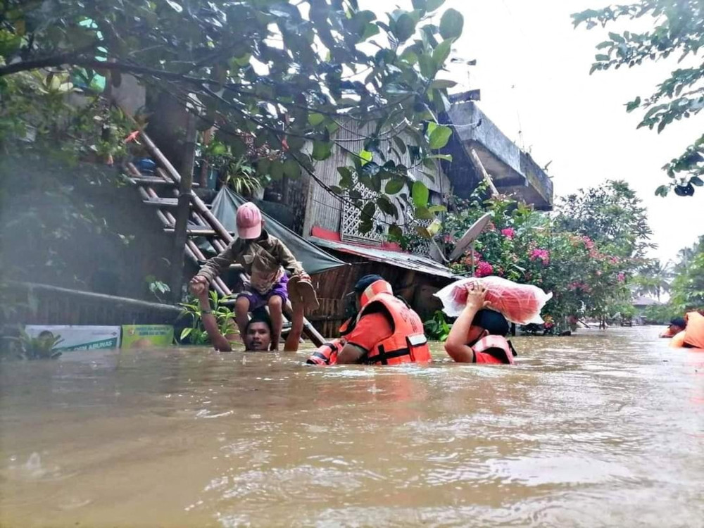 A man carries a boy on his shoulder April 10, 2022, as they walk on a flooded road after Tropical Storm Megi hit Capiz, Philippines. (CNS/Reuters/Philippine Coast Guard Handout)