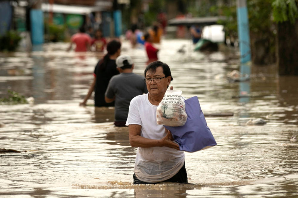 A man carries his belongings through floodwaters Sept. 26, 2022, after Typhoon Noru hit Bulakan, Philippines. Noru left a trail of destruction in northern Philippine provinces and was headed toward Vietnam. (CNS photo/Eloisa Lopez, Reuters)