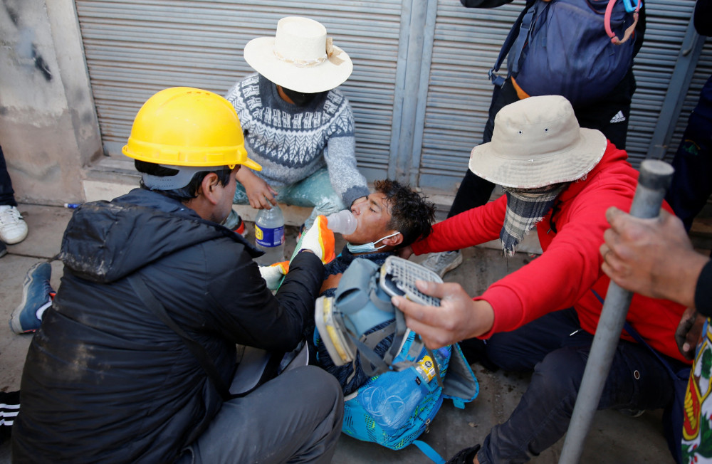 A man wearing a safety helmet holds a breathing device over another man who lays on the ground