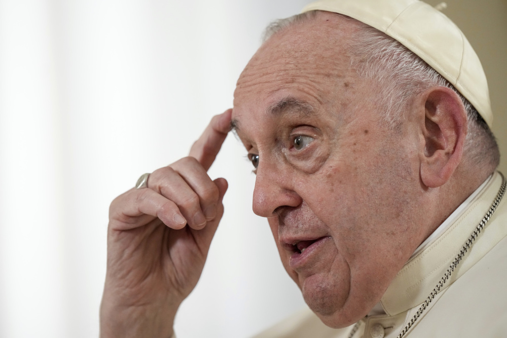 Pope Francis touches a finger to his forehead as he speaks