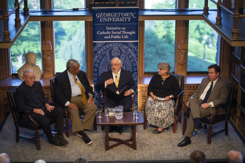 Five adults sit in front of a panel of windows. Panelists are close together and dressed up