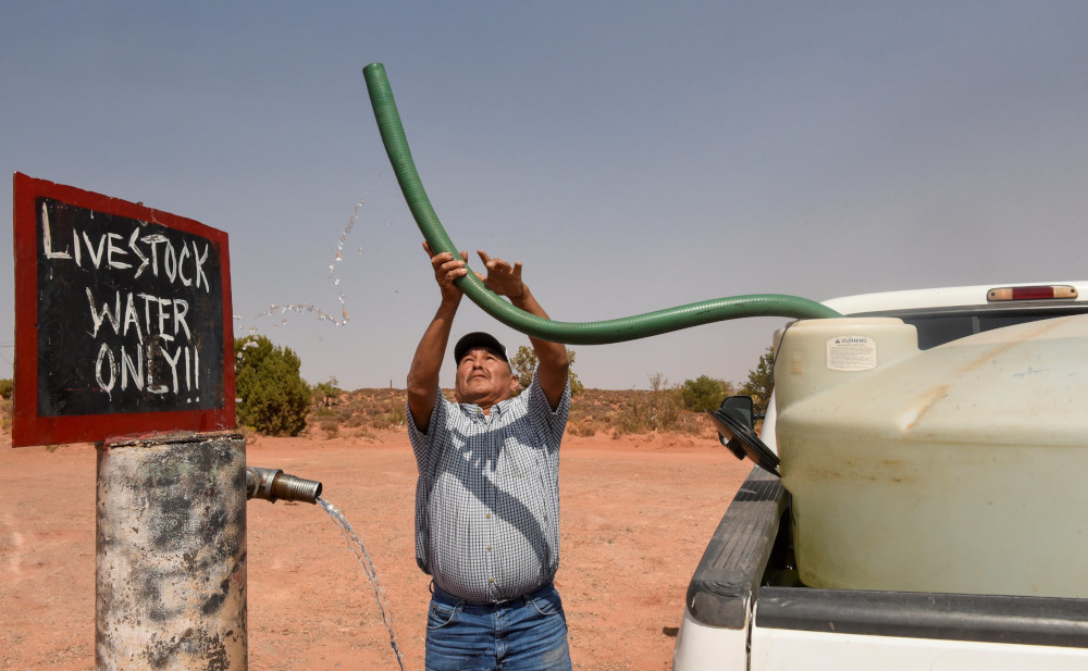 A man holds a tube in the air while standing next to a sign that reads, "Livestock water only."