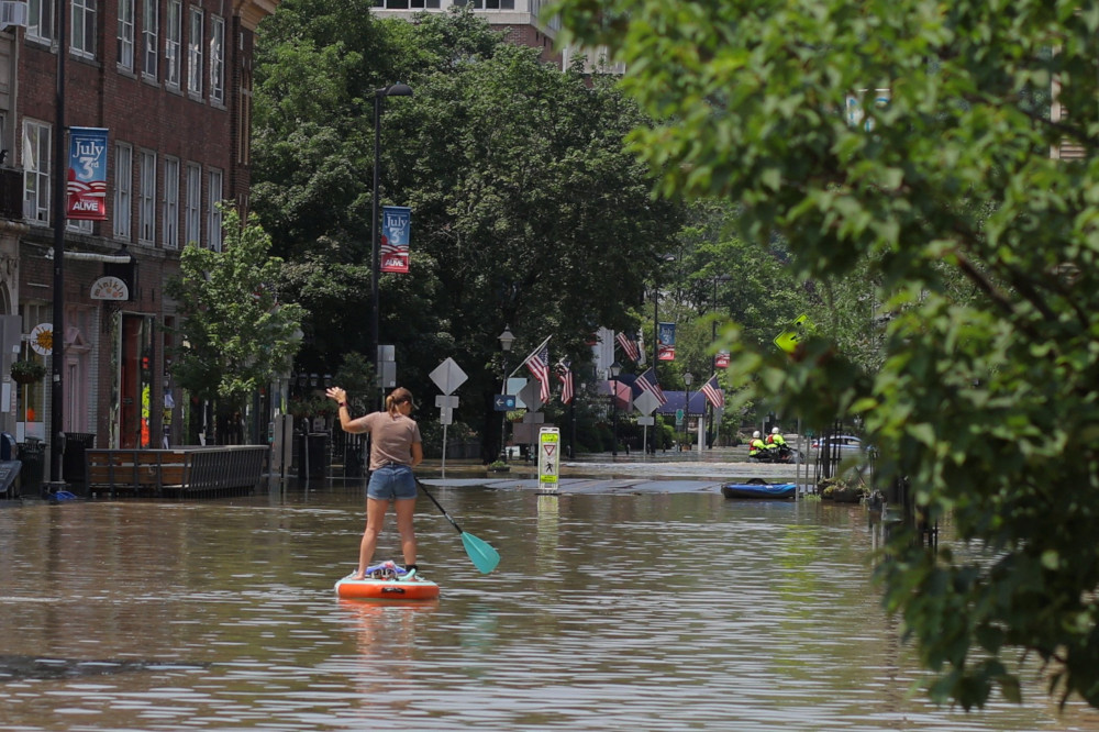 A woman rows a paddleboard down a flooded main street with American flags lining the street