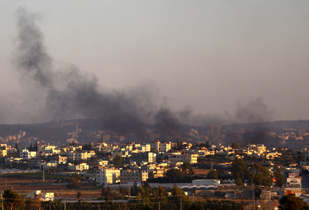 Black smoke billows above buildings and trees set against a dark gray sky