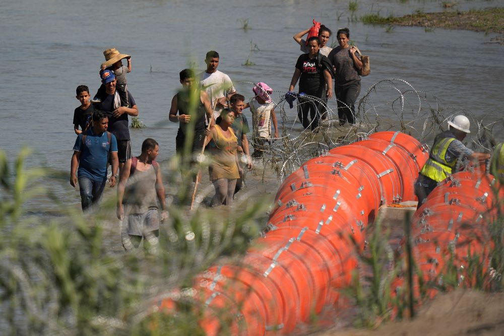 Migrants trying to enter the U.S. from Mexico approach the site where workers are assembling large buoys to be used as a border barrier along the banks of the Rio Grande near Eagle Pass , Texas, July 11. (AP/Eric Gay)