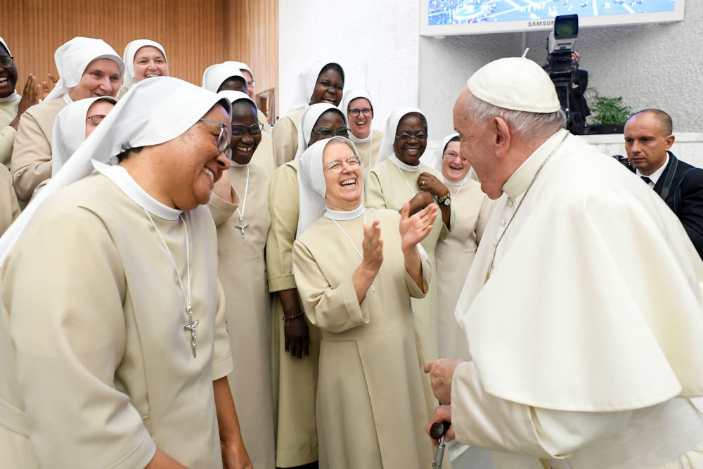 A group of sisters wearing white laugh as they stand in front of Pope Francis