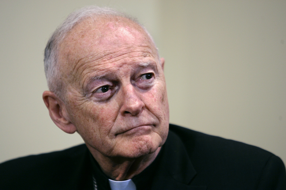 An older white man wearing a clerical collar stares off to the side with a serious expression