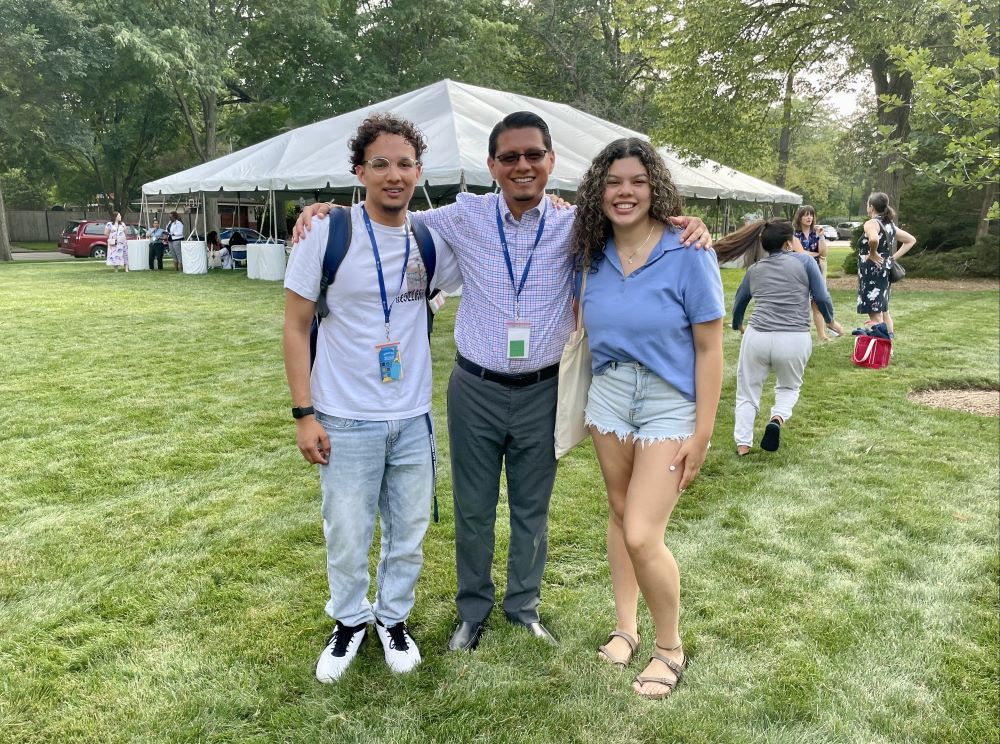 3 people pose, with a large tent in background.