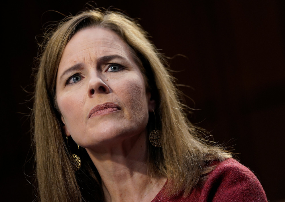 A white woman with shoulder length brown hair wearing a red sweater, dangly earrings and light makeup stares off camera 