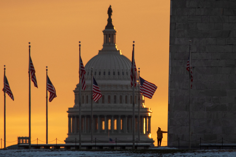 The sky is orange behind the U.S. Capitol dome with American flags flying around it