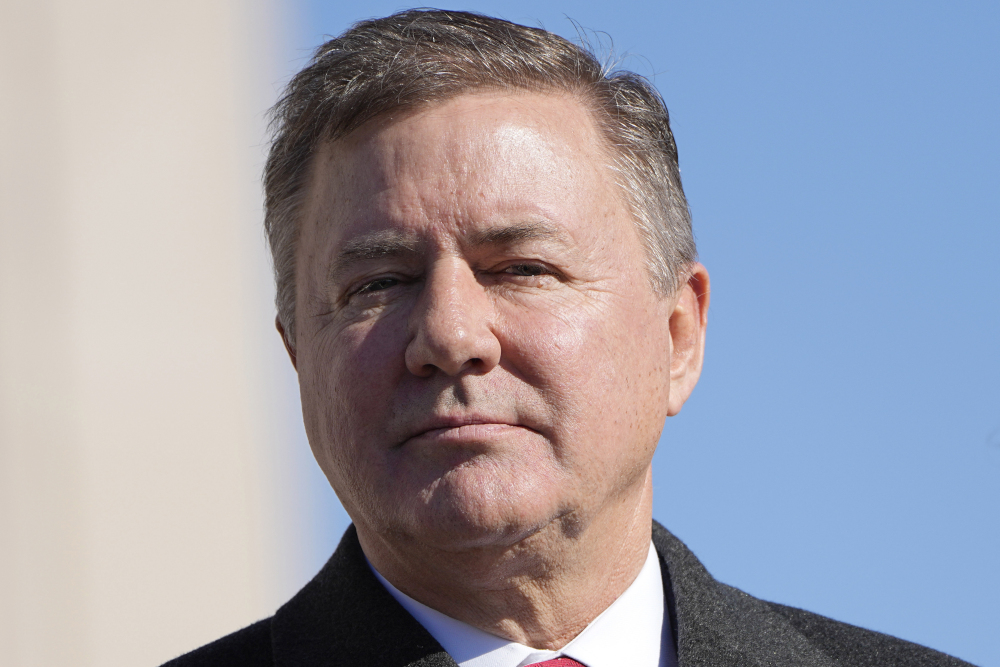 A white man with brown and gray hair wearing a suit is seen from the shoulders up