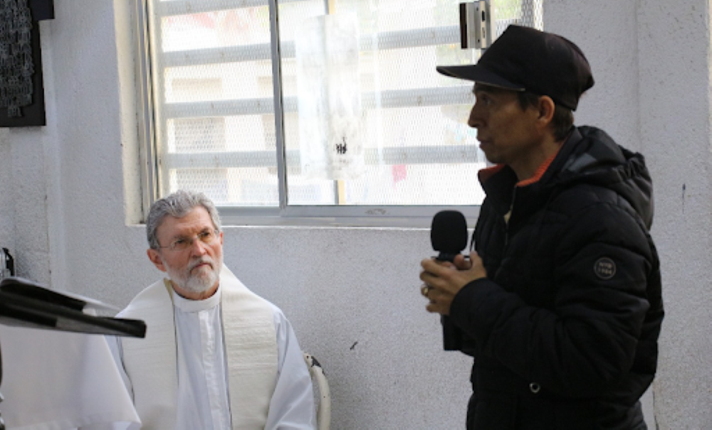 Msgr. Luis Eduardo Villarreal listens during Epiphany Mass at  Casanicolás on Jan. 7 as Carlos describes traveling through the Darien jungle between Colombia and Panama and traveling on the Mexican freight train known as "the beast" or "train of death." 