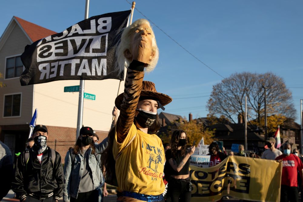 A woman in Detroit carries a mask of President Donald Trump as people march in the street to celebrate on Nov. 7, 2020, after the media announced Democrat Joe Biden had won the presidential election.