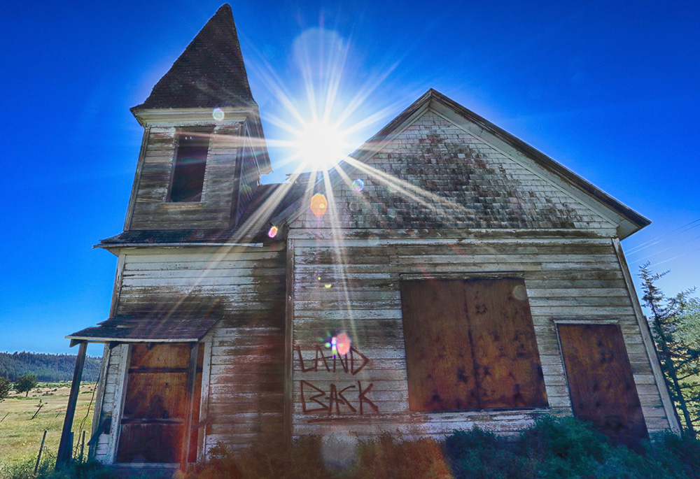 "Land back" is painted on a crumbling, abandoned church located on Oregon's Warm Springs Indian Reservation, June 25, 2022. (Flickr/Ian Sane, CC BY 2.0)