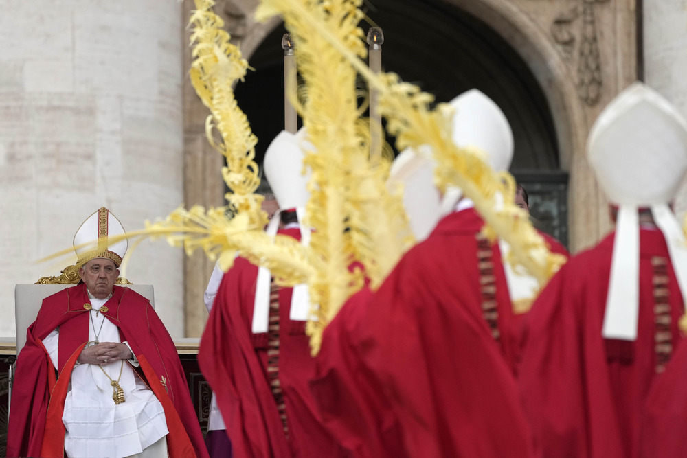 Pope Francis seated, vested for Mass, Bishops process with palms in foreground