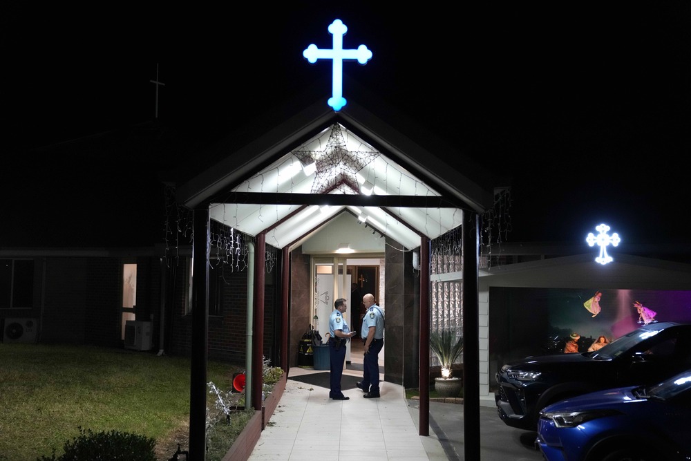 Two law enforcement officer stand beneath church portico at night, illuminated blue cross tops portico.