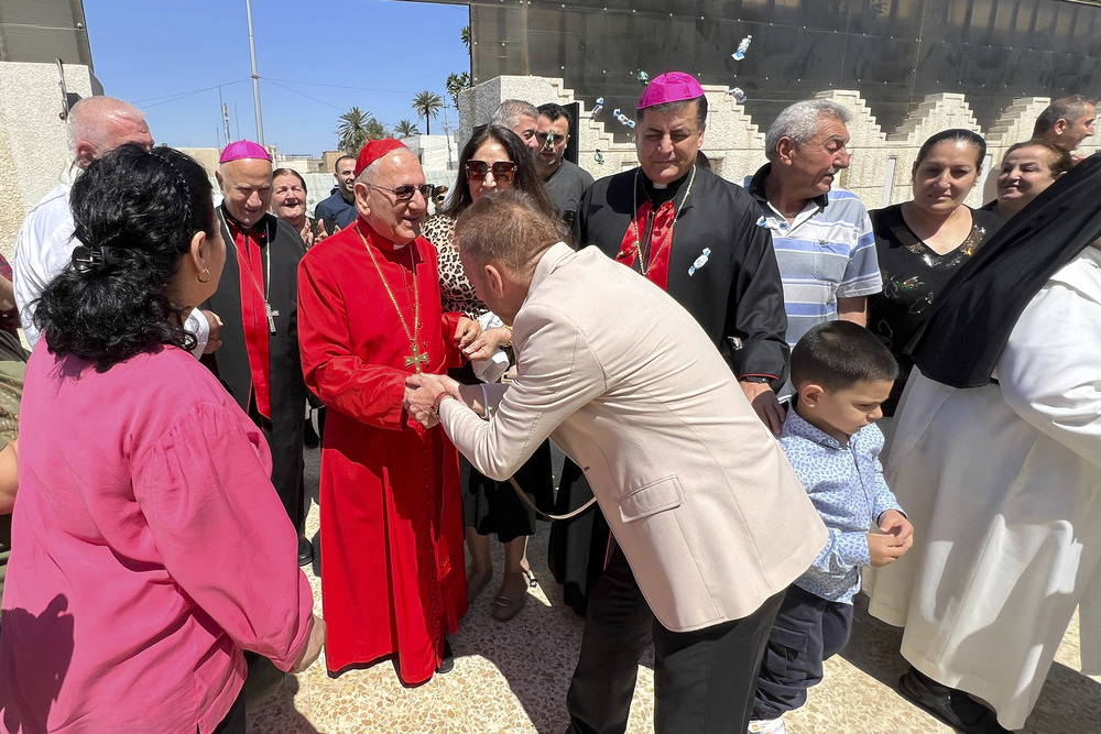 Cardinal, wearing red clerical garb, greets joyful crowd in street. 