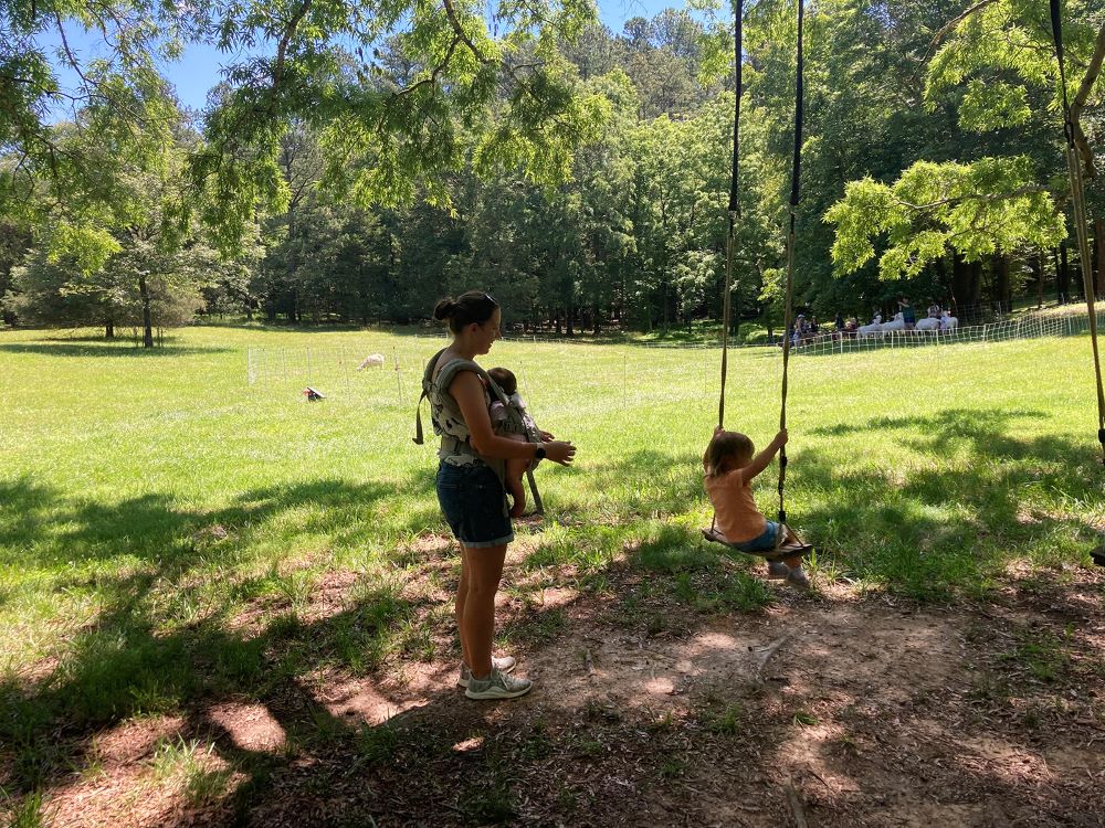 Joan Thanupakorn, of Durham, North Carolina, pushes her daughter, Nora, on a swing hanging from a tree during a Grow It wellness program for children at Spring Forest in nearby Hillsborough, on May 29, 2024. (RNS photo/Yonat Shimron)