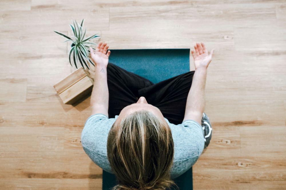 woman sits on cushion, with hands pointing upward