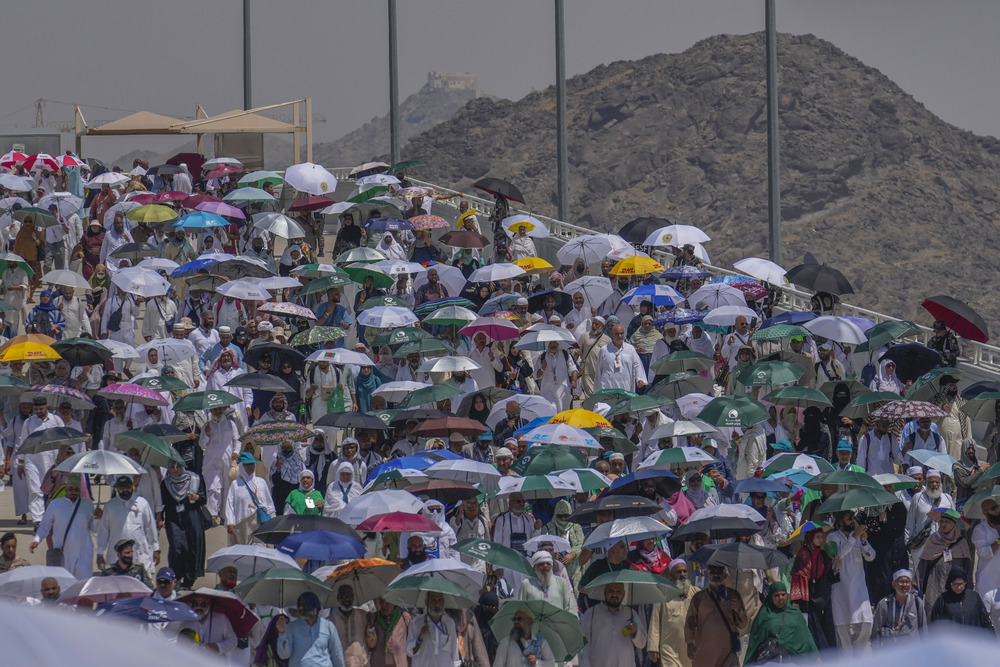 Large crowd pictured under their umbrellas against mountainous, desert terrain. 