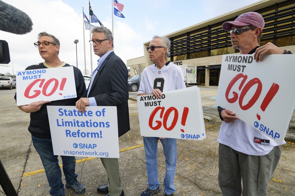 People stand holding signs advocating for statute of limitations reforms