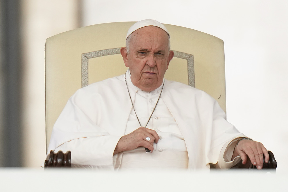 Pope Francis, seated, scowls.