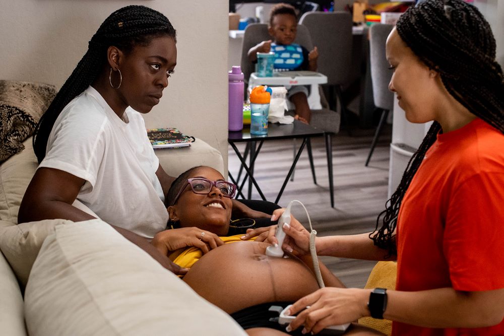 A midwife talks with a woman and her pregnant wife in their home in Fountain Valley, California, in June 2021. In an effort to avoid racism and higher maternal mortality rates, some Black women are turning to Black midwives for care. (Grist/MediaNews Group/Los Angeles Daily News via Getty Images/Sarah Reingewirtz)