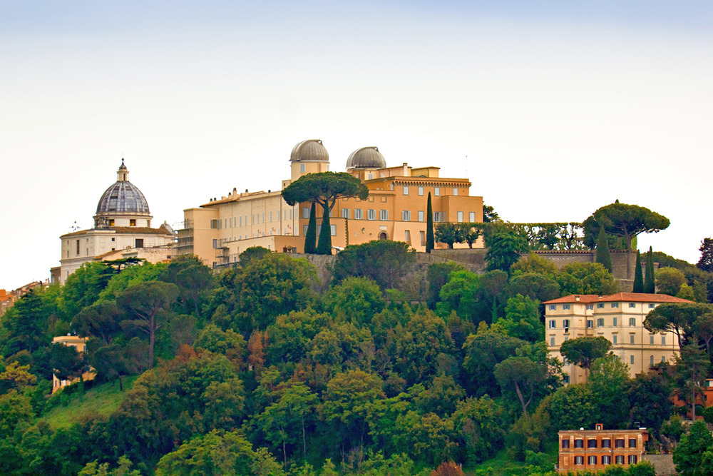 A cluster of large, romanesque buildings sits stop a verdant hill