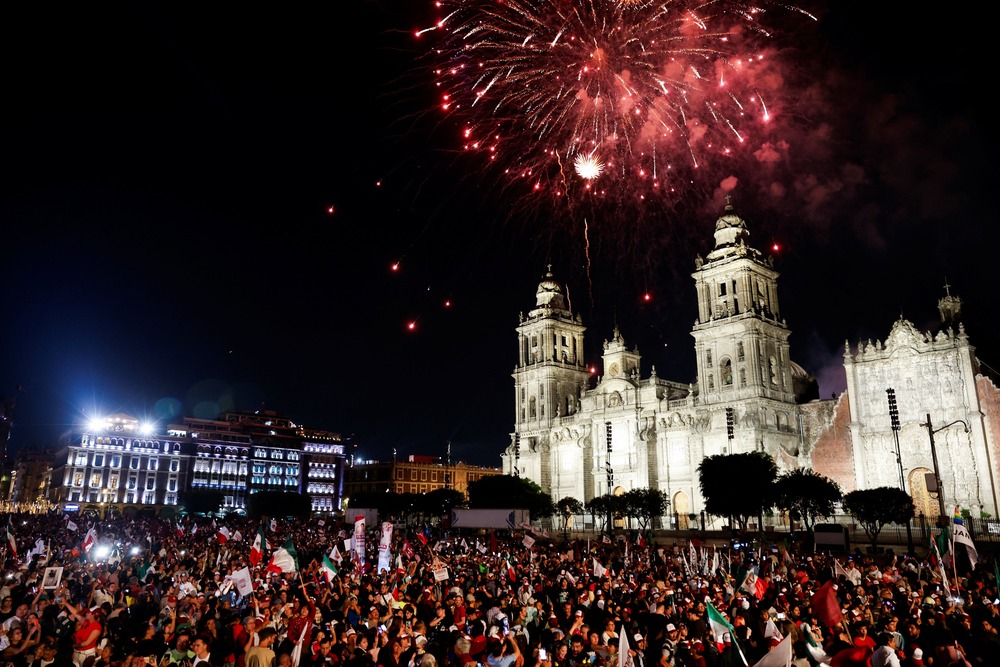 Fireworks explode in night sky over large crowd assembled in front of the Metropolitan Cathedral. 