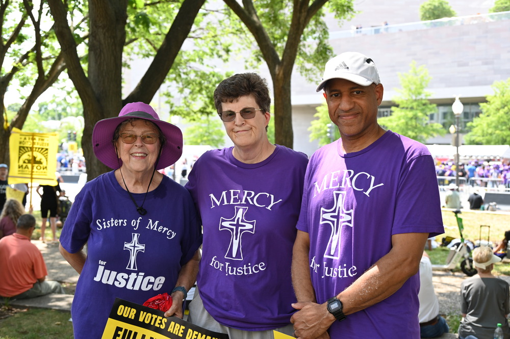 Three people in a row, wearing purple Sisters of Mercy of shirts