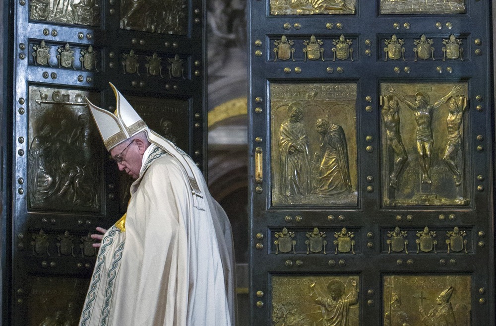 Pope Francis, vested, stands in monumental doorway, preparing to shut doors. 