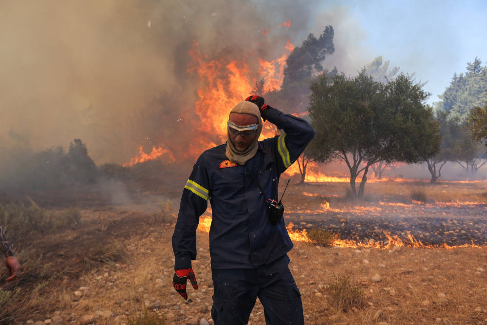 A firefighter walks next to rising flames as a wildfire burns near the village of Vati, on the island of Rhodes, Greece, July 25, 2023. Extreme heat waves in summer 2023 saw Greece, Italy and Spain record all-time high temperatures with the heat index in several Middle Eastern countries reaching 152 degrees Fahrenheit, near the limit of human survival. (OSV News photo, Nicolas Economou, Reuters)