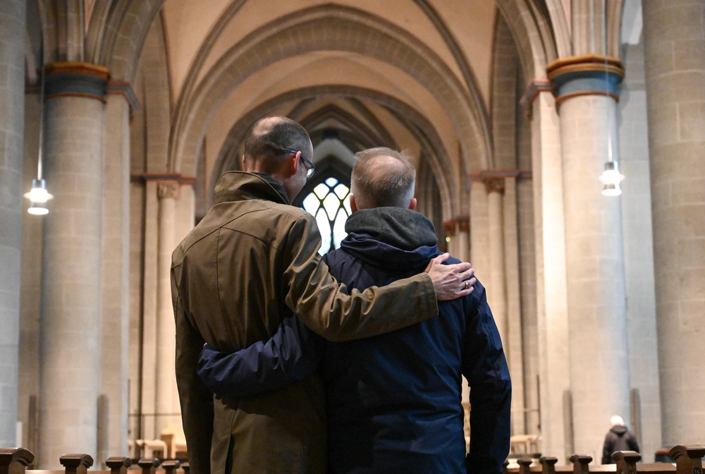 Two men pictured from behind with arms on each other's shoulder. 