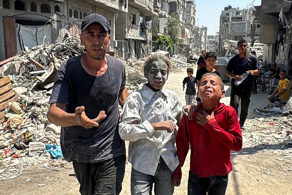 A man and two children walk through rubble; one child's face is completely white with dust, and the other sobs. 