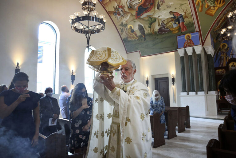 Vested priest processes down aisle of church holding up a sacred item.