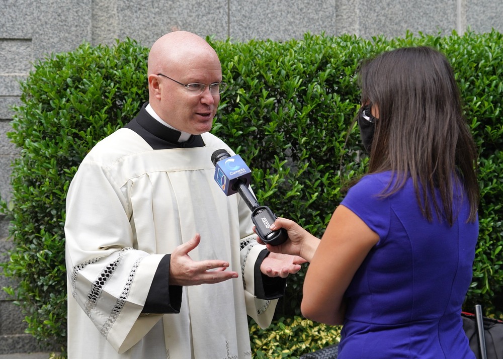 Landry, in choir dress, speaks outdoors to reporter.  