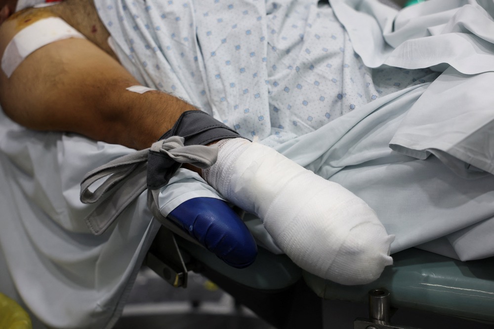 Bandaged arm seen along with bruised upper arm with medical tape applied; patient's face not shown, only gowned torso.