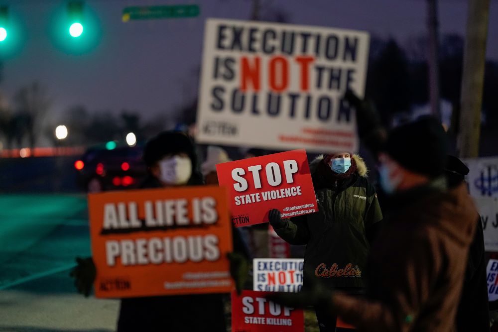 Demonstrators gather outside the federal prison in Terre Haute, Indiana, holding signs opposing the death penalty.