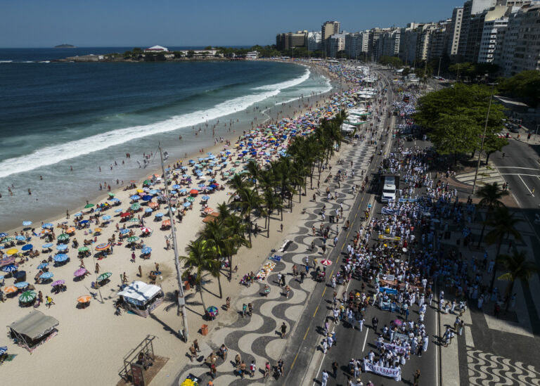 Aerial view of large assembly marching alongside beach. 