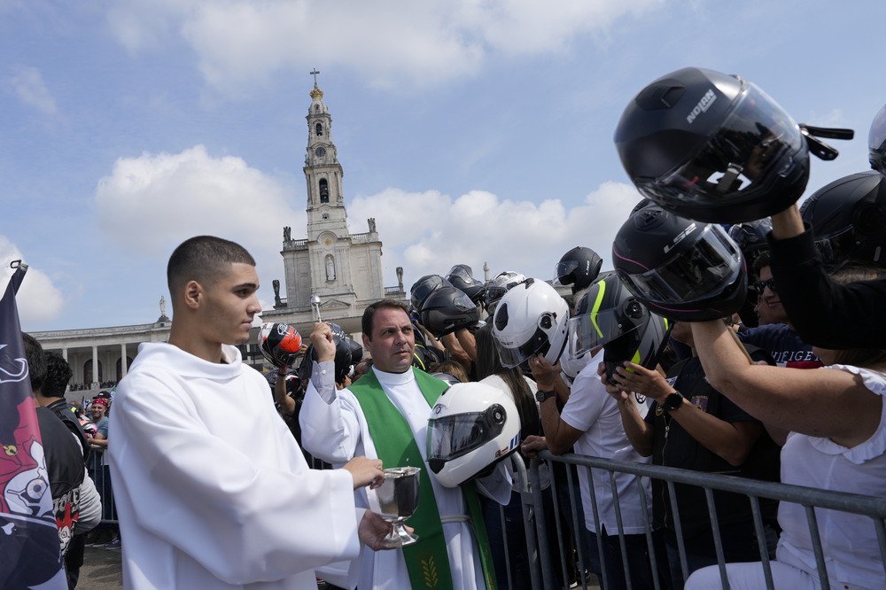 Priest flings holy water and crowd of bikers holding their helmets up.