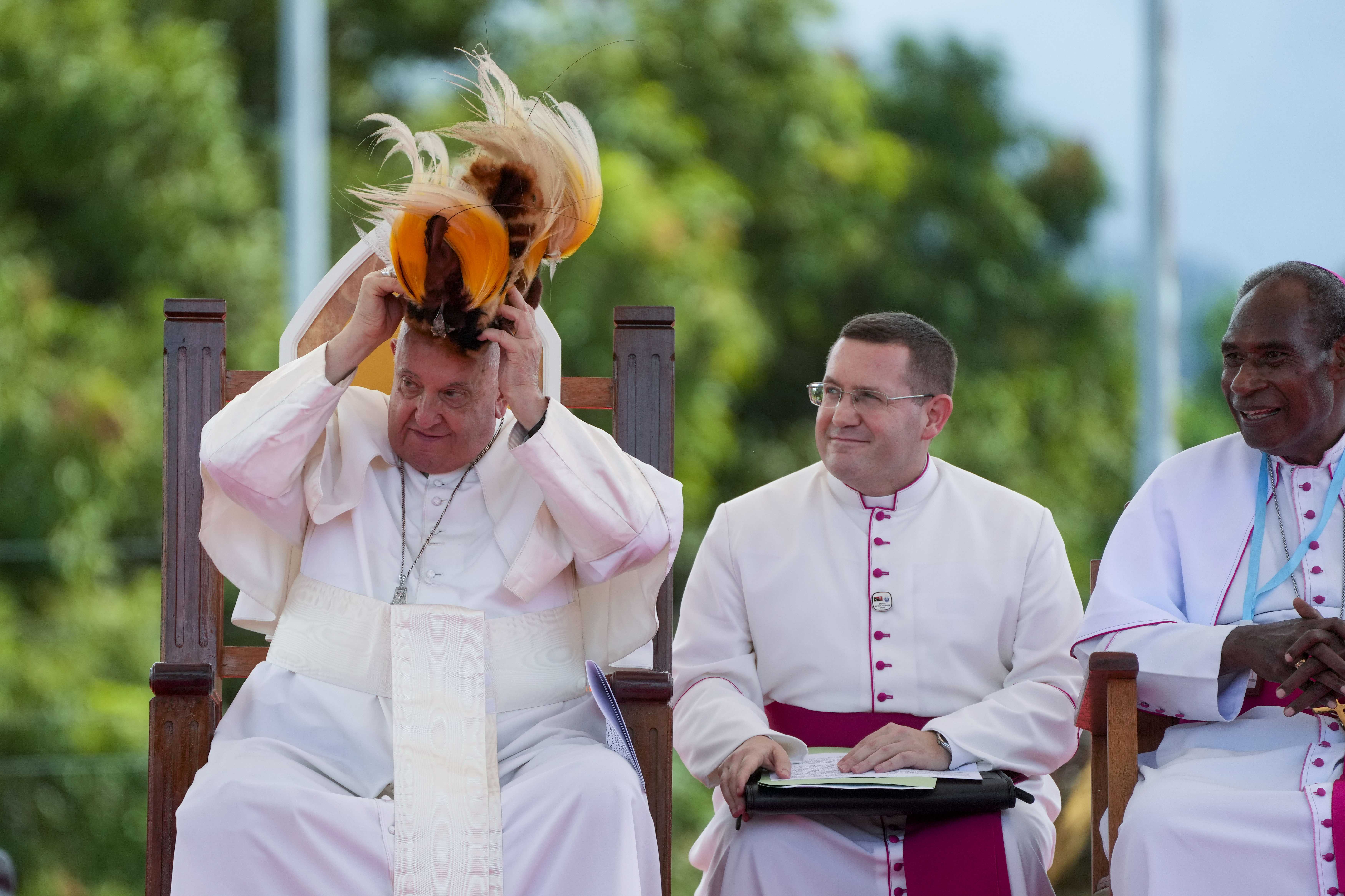 Pope Francis receives a traditional hat during a meeting with faithful in Vanimo, Papua New Guinea, Sunday, Sept. 8, 2024. Pope Francis celebrated the Catholic Church of the peripheries on Sunday as he traveled to the remote jungles of Papua New Guinea, bringing with him a ton of medicine and toys and a message of love overcoming violence for the people who live there. At right is Vanimo Bishop Francis Meli. (AP Photo/Gregorio Borgia)