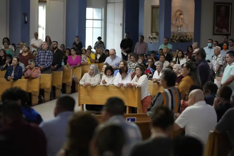 People in pews praying in a very full church.