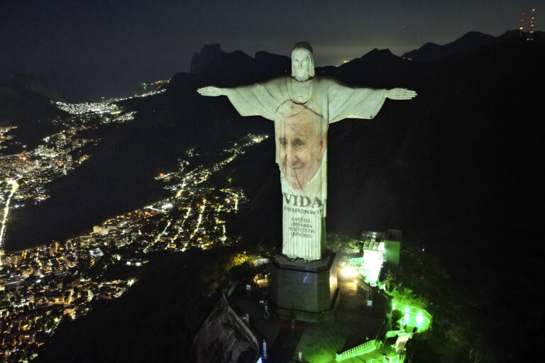 Pope Francis' face projected at night onto monumental statue. 