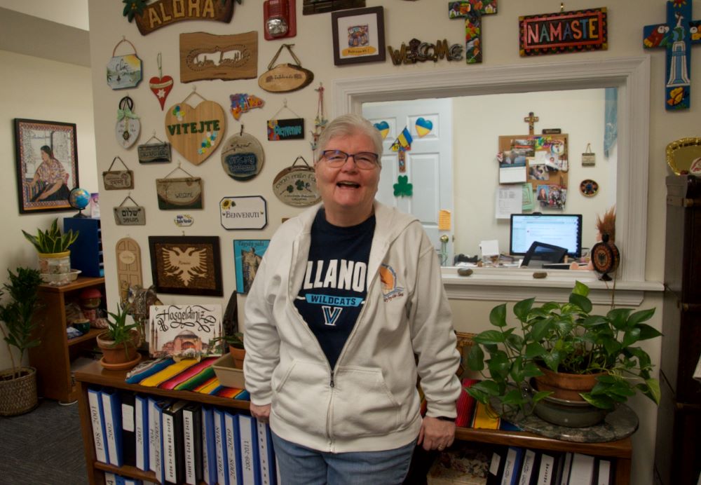 Sr. Pat Madden stands before a wall covered with welcome signs given by clients the Sisters of St. Joseph Welcome Center has helped with literacy and citizenship classes. 