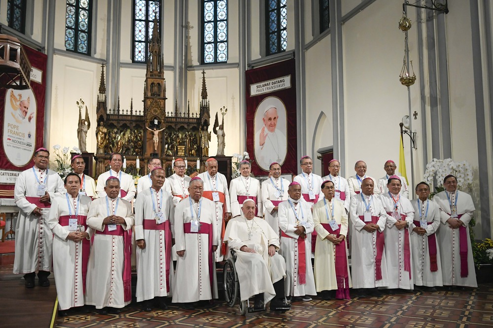 Two rows of cardinals stand in front of altar and behind Pope Francis, seated in wheelchair.