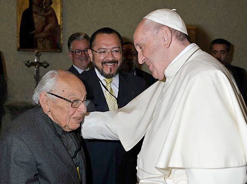 Francis smiles and puts his hand on Gutiérrez's shoulder. Gutiérrez is seated.