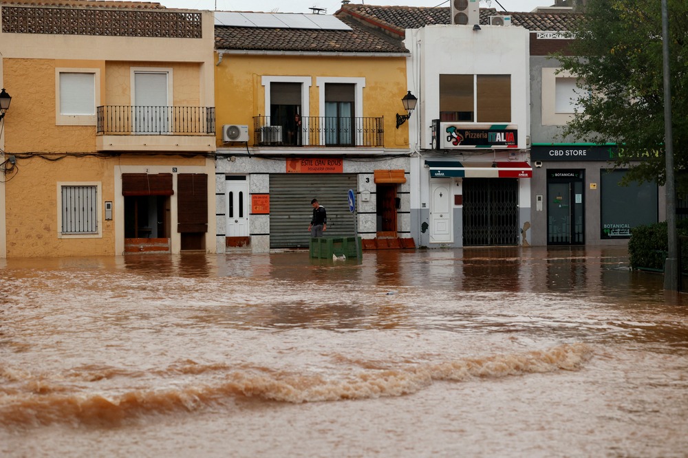 Street runs with a river of brown water past low, attached buildings.